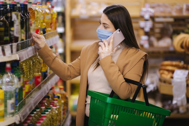 Donna in maschera protettiva parla al telefono in supermercato a scegliere groseries