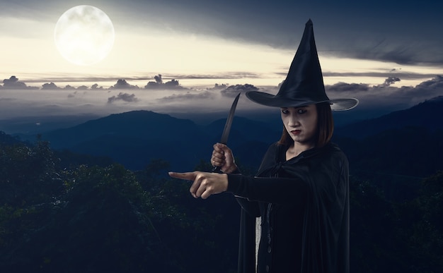 Donna in nero spaventoso strega costume di halloween In possesso di un coltello con moonlight montagna e s