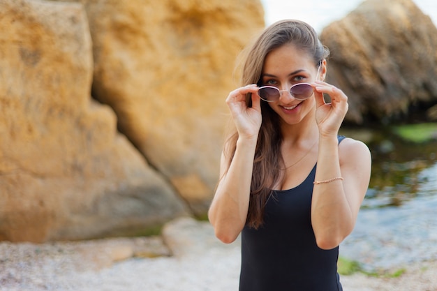 donna in occhiali da sole sorridente su una spiaggia selvaggia con pietre