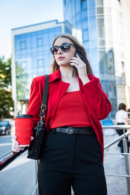 Donna in occhiali e abiti classici di marca che tiene una tazza di caffè e sorride sulla città