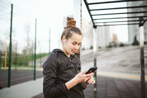 Donna in palestra all'aperto con cuffie e smartphone.