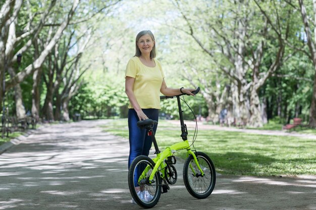 Donna in pensione che riposa nel parco Una donna persiana dai capelli grigi cammina con una bicicletta in una giornata estiva