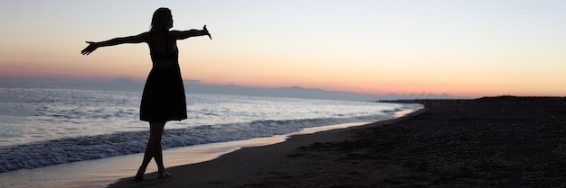 Donna in piedi a braccia aperte in riva al mare al tramonto