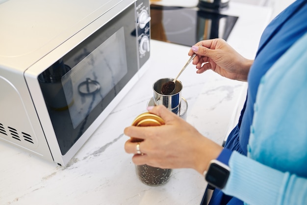 Donna in piedi al bancone della cucina in ufficio e mettendo un cucchiaio di caffè macinato in tazza