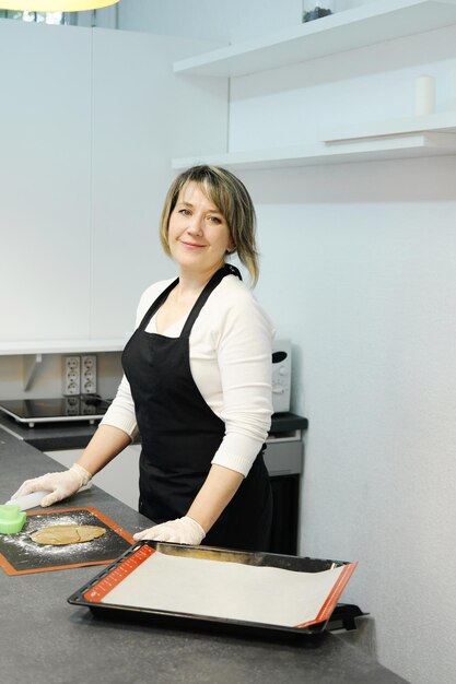 Donna in piedi in cucina bianca e guardando la telecamera nel suo laboratorio di torte Concetto di piccola impresa Foto verticale