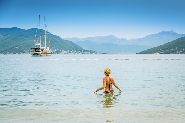 Donna in piedi nel mare e guardando lo yacht