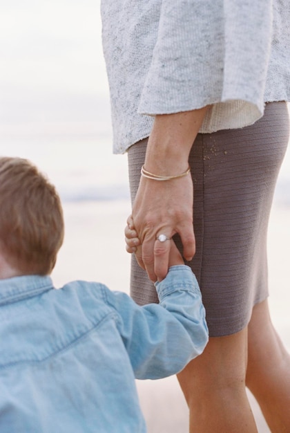 Donna in piedi su una spiaggia sabbiosa in riva all'oceano che tiene la mano del suo giovane figlio