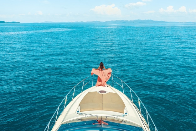 Donna in piedi sulla prua di uno yacht in una soleggiata giornata estiva, brezza di capelli in via di sviluppo, bel mare in superficie