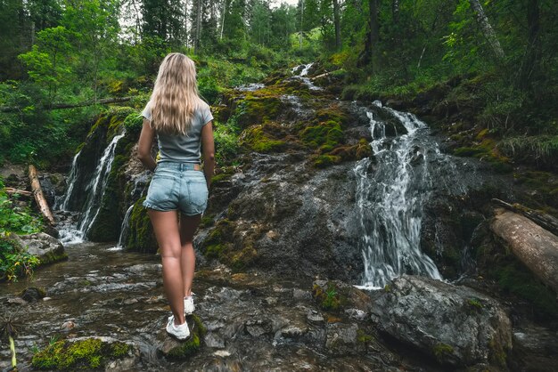 Donna in piedi sulla roccia e godersi la vista della cascata. Altai, Siberia. vista da dietro