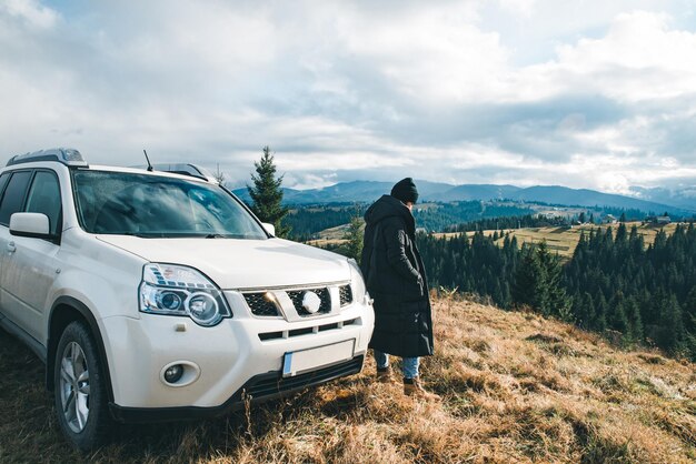 Donna in piedi vicino a un'auto suv al picco di una collina guardando la splendida vista del viaggio su strada delle montagne