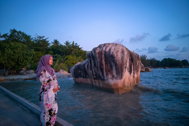 Donna in piedi vicino a una roccia sulla spiaggia contro il cielo blu
