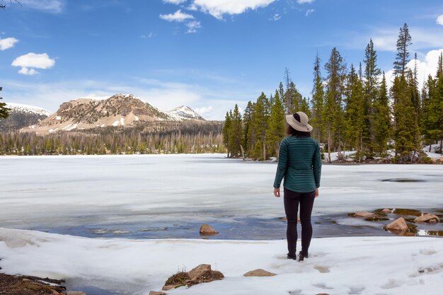 Donna in piedi vicino al lago innevato circondato da alberi e montagne