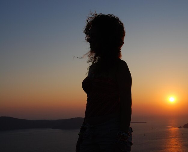Donna in piedi vicino al mare contro il cielo durante il tramonto