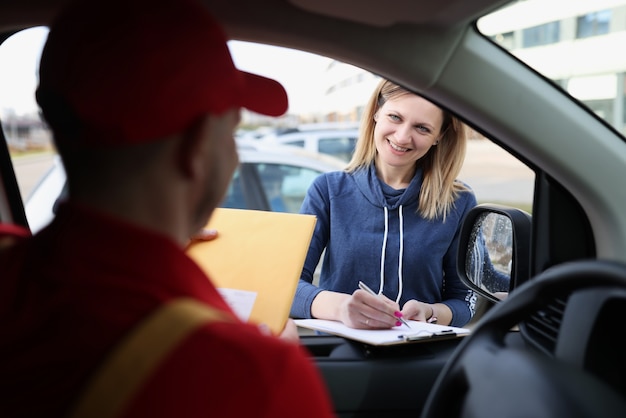 Donna in piedi vicino all'auto con il corriere e firma la ricevuta di consegna