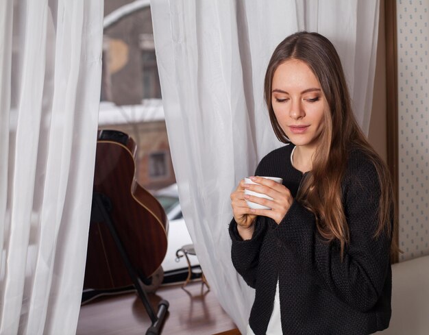 Donna in piedi vicino alla finestra e bere caffè