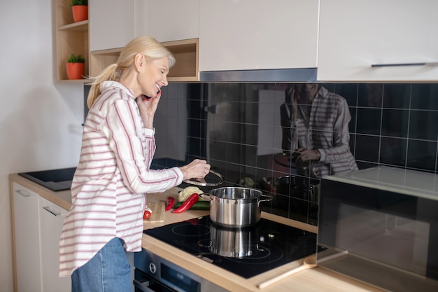 Donna in piedi vicino alla stufa in cucina e parlando al telefono