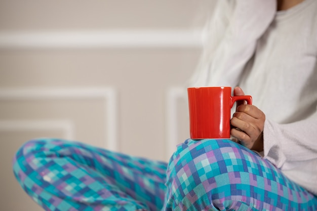 donna in pigiama che tiene una tazza di caffè rossa