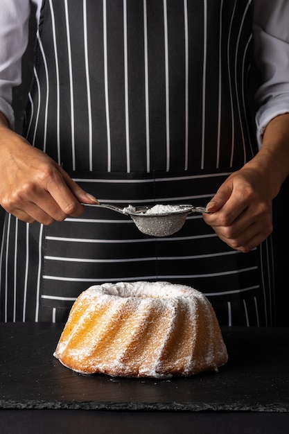 Donna in polvere di zucchero per ciambellone alla vaniglia su sfondo scuro.