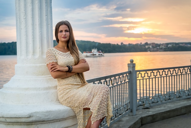 Donna in posa seduta sulla colonna sulla riva del lago. Paesaggio urbano