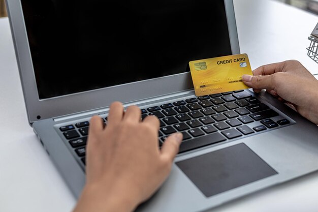 Donna in possesso di carta di credito e digitando sulla tastiera di un laptop, sta compilando i dati della carta di credito per pagare un ordine su un sito di acquisti su Internet. Shopping online e concetto di pagamento con carta di credito