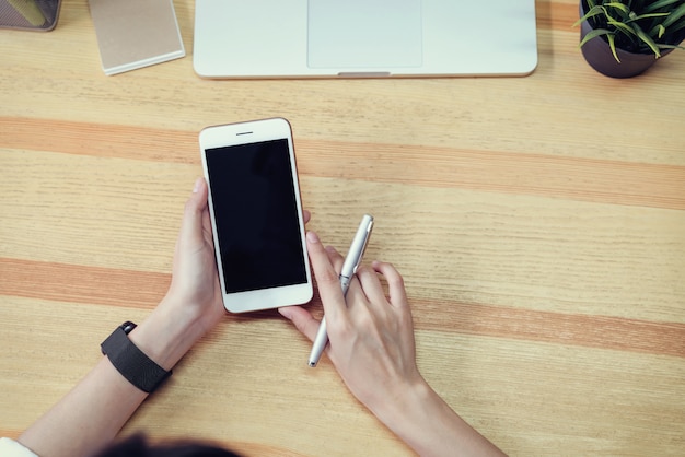 Donna in possesso di un telefono schermo vuoto e un computer portatile e mettere un orologio intelligente, effetto pellicola.