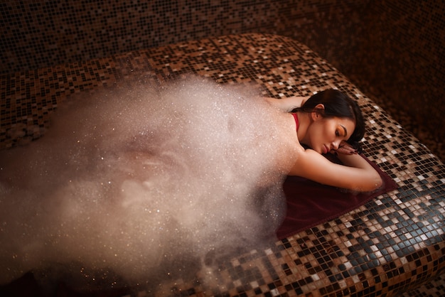 Donna in schiuma sdraiata su una pietra calda, bagno turco, hammam, sauna