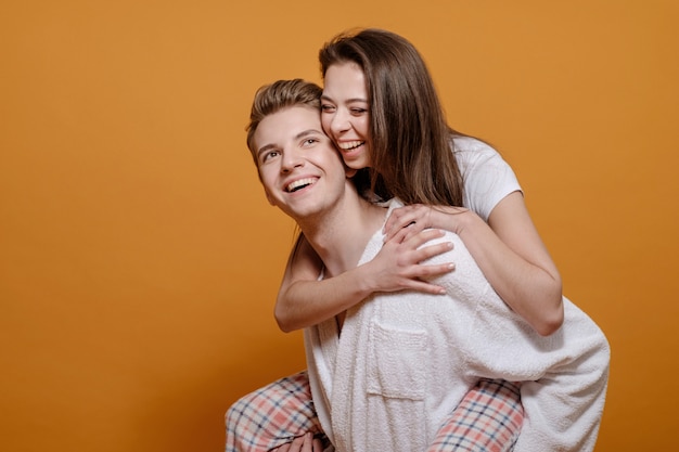 Donna in sella a un fidanzato, coppia sposata in abiti domestici su sfondo giallo, relazione felice, giovane donna abbraccia l'uomo