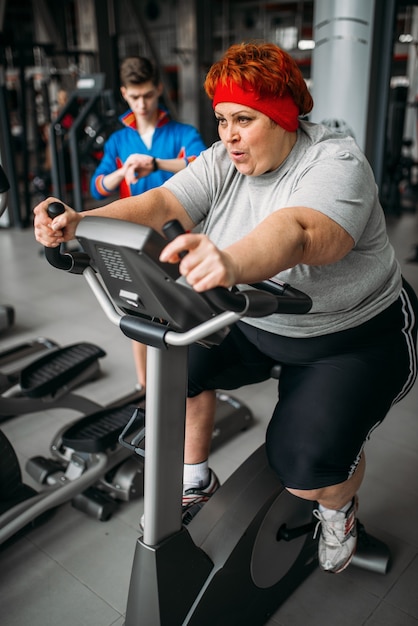 Donna in sovrappeso, allenamento sulla cyclette in palestra. Calorie che bruciano, persona di sesso femminile obesa nel club sportivo, persone grasse