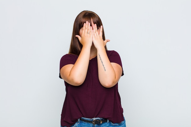 Donna in sovrappeso che copre il viso con le mani, sbirciando tra le dita con espressione sorpresa e guardando di lato