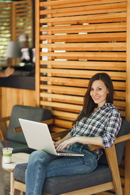 Donna in strada all'aperto estate caffetteria caffè in legno seduto in abiti casual, lavorando su un moderno computer pc portatile, rilassante durante il tempo libero. Ufficio mobile