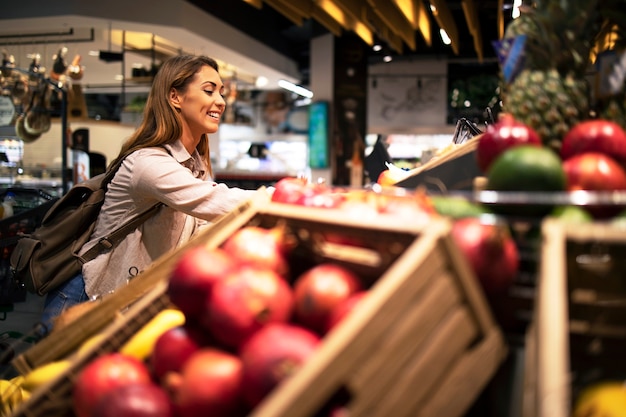 Donna in supermercato scegliendo la frutta più deliziosa al negozio di alimentari del reparto frutta.