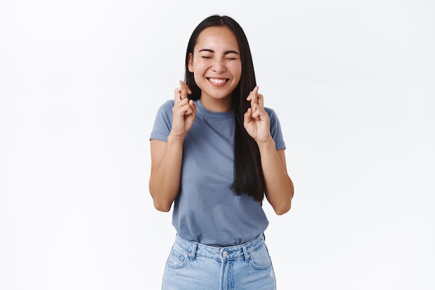 donna in t-shirt, jeans, occhi chiusi e sorridente eccitata come esprimere un desiderio, incrociare le dita buona fortuna, il sogno diventa il numero uno