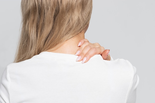 Donna in top bianco con dolore al collo e alla schiena.