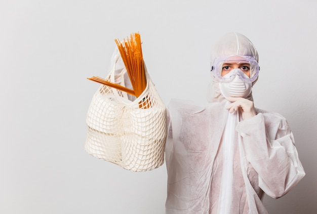 donna in tuta protettiva e occhiali con maschera tiene carta igienica e pasta