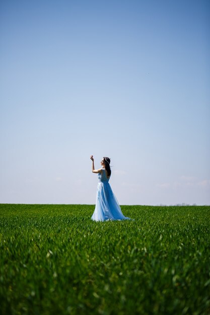 Donna in un abito lungo blu su uno sfondo di campo verde. Ritratto di moda di una bella ragazza con un sorriso sul viso