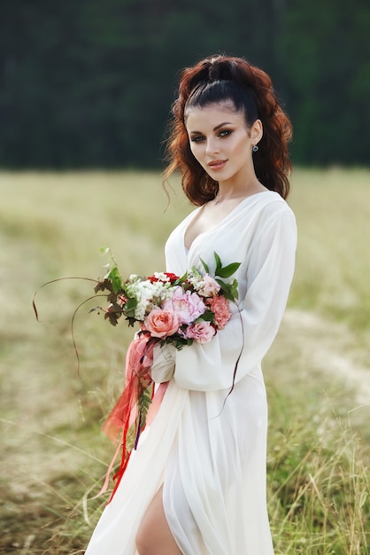 donna in un abito lungo si trova in un campo con ghirlanda in testa e bouquet di fiori in mano, bella donna sotto i raggi del sole della sera in autunno nel villaggio. Rurale