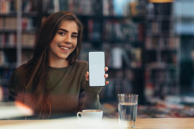 Donna in un caffè che tiene e mostra lo schermo bianco dello smartphone