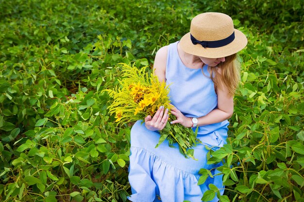 donna in un campo verde si siede con un mazzo di fiori selvatici