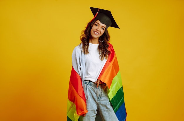 donna in un cappello di laurea in posa con la bandiera arcobaleno Lgbt su giallo