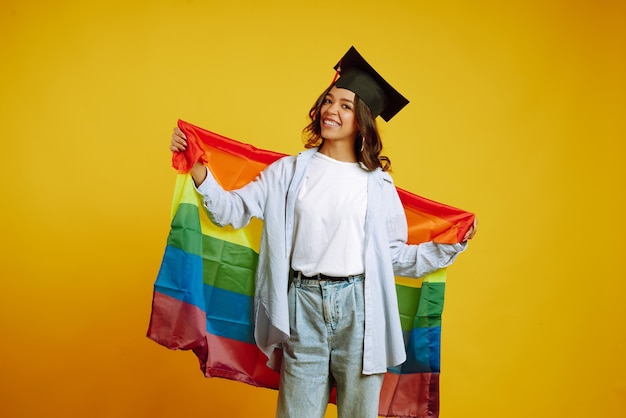 donna in un cappello di laurea in posa con la bandiera arcobaleno Lgbt su giallo