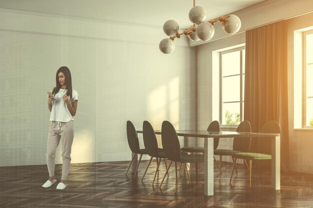 Donna in un interno minimalista della sala da pranzo con pavimento in legno scuro, pareti bianche, grandi finestre con tende e tavolo con sedie verdi. Il rendering 3d simula la doppia esposizione dell'immagine tonica