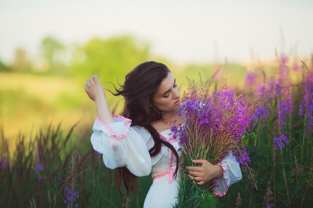 Donna in un lungo abito bianco, accarezzando i capelli lunghi, in piedi in un campo di lavanda