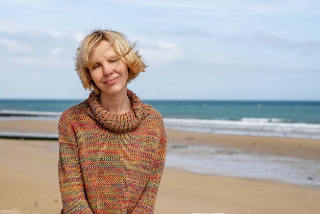 Donna in un maglione sul mare dell'oceano Attraente donna di mezza età con i capelli mossi dal vento sorridente Soleggiato riposo relax in vacanza Posto per il testo