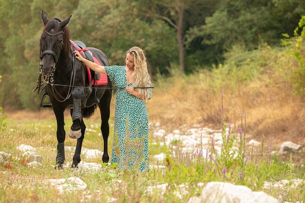 Donna in un vestito con un cavallo nero nella natura