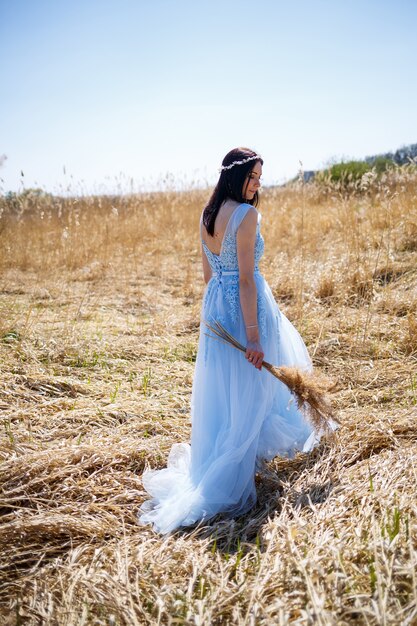 Donna in un vestito lungo blu tra le canne. Ritratto di moda con fiori secchi