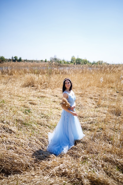 Donna in un vestito lungo blu tra le canne. Ritratto di moda con fiori secchi