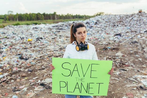 Donna in una discarica volontaria con in mano un poster per salvare la terra