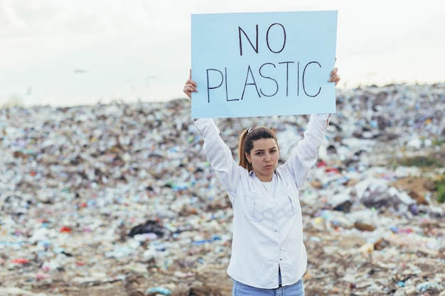 Donna in una discarica volontaria con in mano un poster per salvare la terra