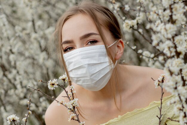 donna in una maschera medica. donna in primavera tra il giardino fiorito.