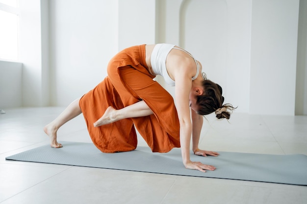 Donna in una postura dinamica di yoga su un tappetino indossando pantaloni arancioni e un top bianco che pratica la consapevolezza